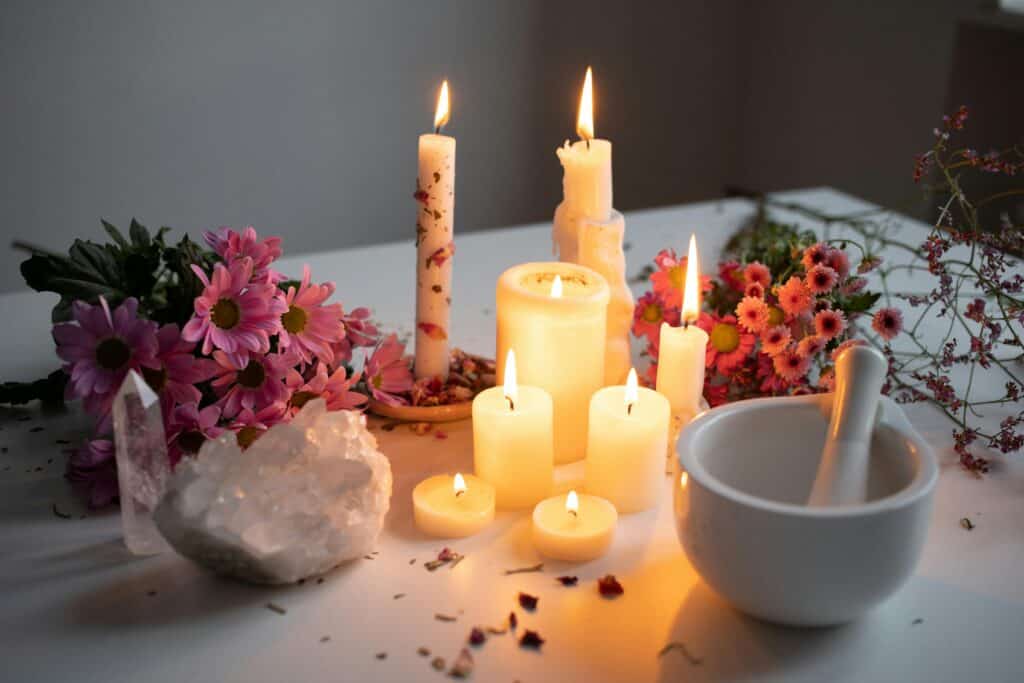 A tranquil aromatherapy scene featuring lit candles, pink flowers, and crystal accents on a white desk.